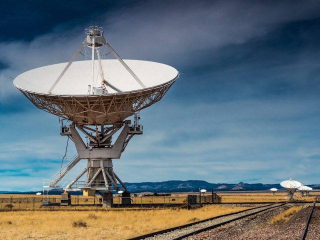 A satellite dish on a rural Indonesian island connects a village to the internet, with technicians installing equipment nearby.
