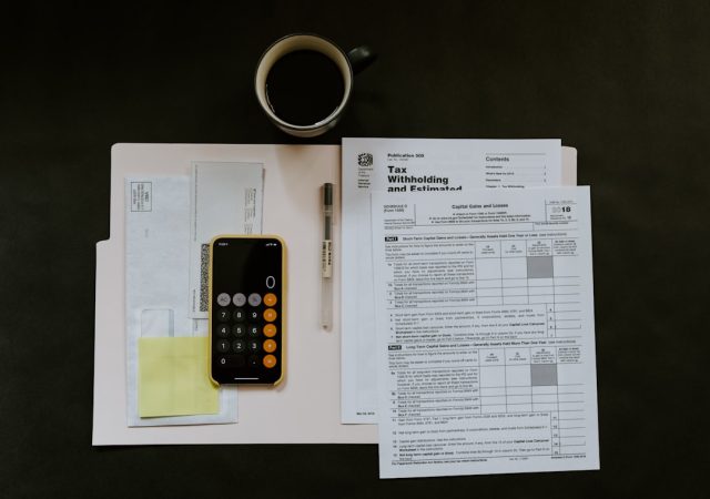 Indiana businesses owe taxes already paid after payroll fraud probe A stack of tax forms and a calculator on a desk, with a blurred office background suggesting a small business setting.