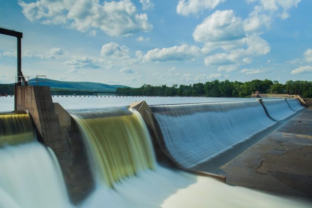 Three operational Vietnamese hydropower stations with water flowing through turbines under a bright sky.