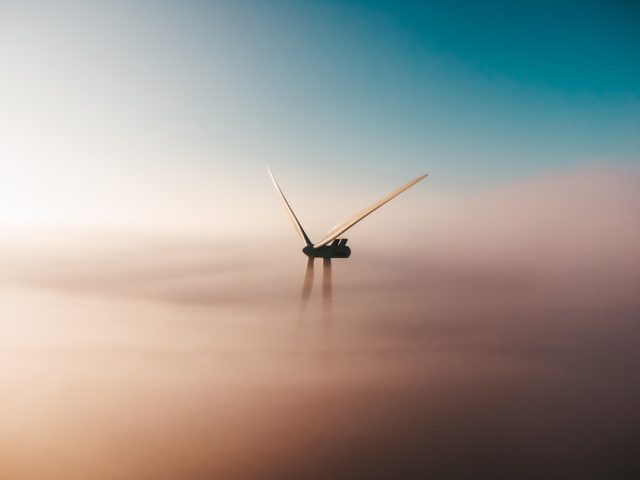 Wind turbines spin on a grassy hill under a blue sky, symbolizing renewable energy growth in the United States.
