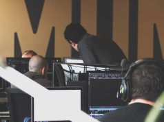 ShinyHunters Claims Aura Breach, 900,000 Records Leaked Hacker wearing headset speaks into phone while typing on laptop, digital lock icons float in dark background.