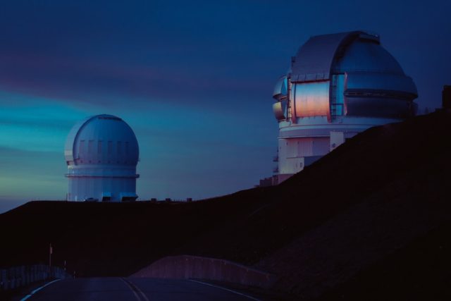 A cosmic ray detection observatory in the Utah desert under a starry night sky, with a particle trail streaking toward the ground.