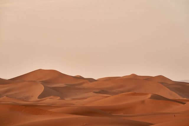Aerial view of a shallow grave in the Libyan desert, with scattered belongings and footprints marking the site where 65 migrant bodies were found.
