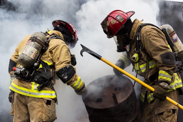 Firefighters and emergency vehicles at the site of a building fire in Hyderabad, with smoke rising over the Hussain Sagar lake.