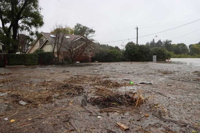 Floodwater surges through a muddy Eastern Cape settlement, washing away makeshift homes and leaving debris along cracked roads.