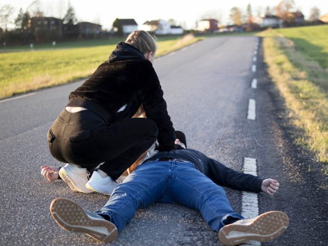 Crashed pickup truck lies on its side beside a rural road as rescue workers tend to victims.
