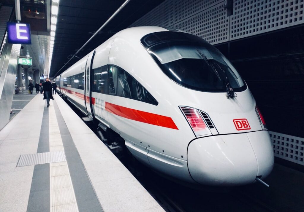 A high-speed train speeds past green Indonesian countryside, with passengers boarding at a modern station.