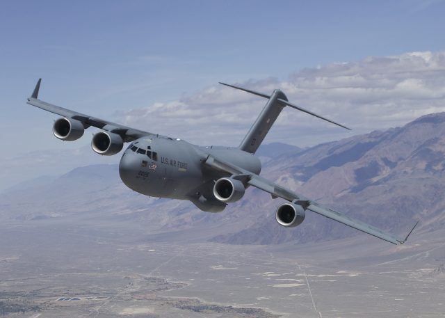 A C-17 Globemaster III opens its rear ramp to release aid bundles over a crowded Gaza neighborhood.