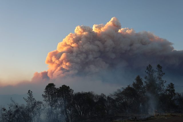Aerial view of the Park Fire burning through rugged terrain and forest in Northern California, with smoke plumes rising over the landscape.