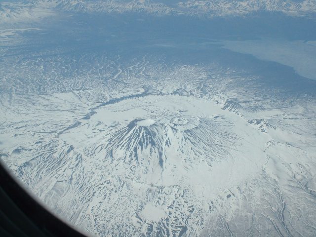 Aerial view of Krasheninnikov volcano erupting on Russia's Kamchatka Peninsula, with ash plume rising above the snow-capped caldera.