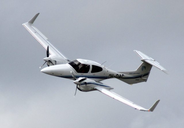 A Diamond DA42 Twin Star aircraft sits on a tarmac at Parafield Airport, with a hangar in the background.