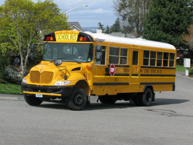 School Bus Crash in England Leaves Two Dead, 17 Injured Overturned yellow school bus on a road in The Wirral, England, with emergency responders and debris visible around the crash site.