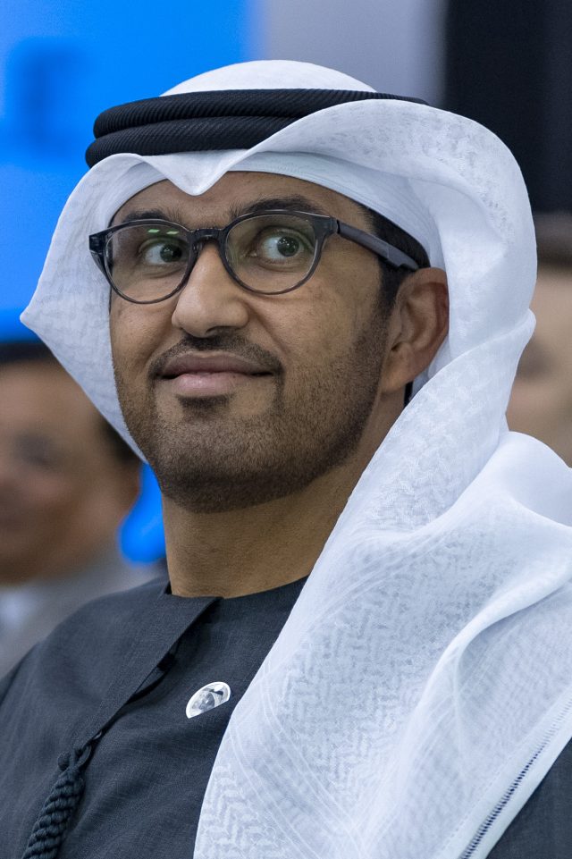 Sultan Al Jaber speaking at a podium during the COP28 climate talks, with delegates in the background.