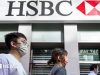 HSBC Hit With Tens of Millions in FCA AML Penalties HSBC headquarters entrance with London City workers passing penalty headlines on phone screens.