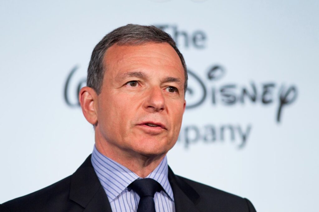 Bob Iger speaking at a Disney event, with a Disney logo in the background.
