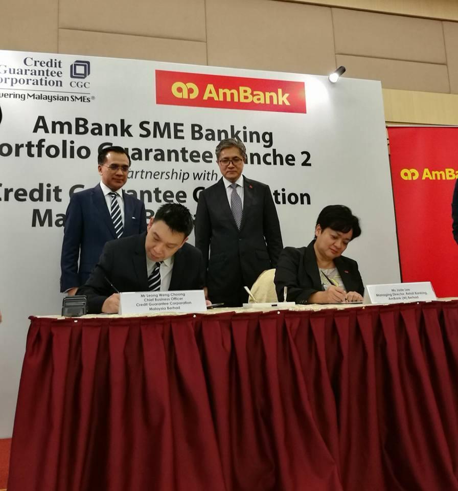 AmBank and PUMM officials shake hands at a signing ceremony in Kuala Lumpur, with documents and a bank logo visible on the table.
