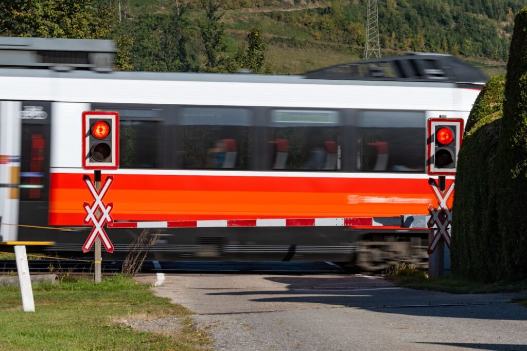 A freight train stands at a level crossing in Thailand, with warning lights and barriers visible near the tracks.