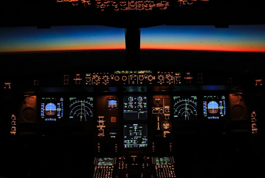 Technician uploads new code to an A320 cockpit computer inside a dim hangar while the jet’s tail fin glows under bright hangar lights.